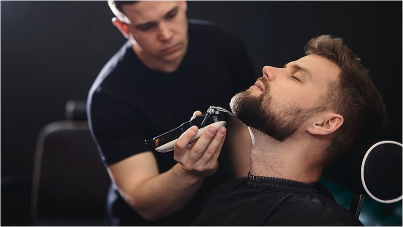 Получение идеальной формы. Крупным планом вид сбоку молодой бородатый мужчина стрижка бороды парикмахер или парикмахер в парикмахерской