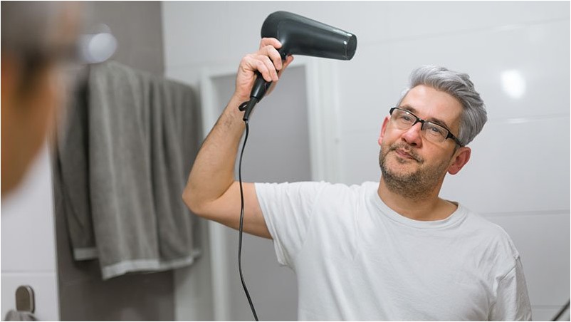 Среднего возраста человек сушит волосы в ванной с феном