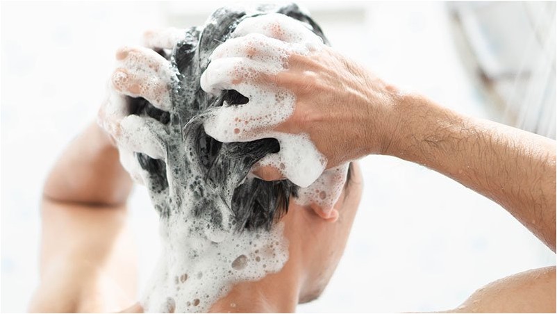 Крупным планом молодой человек, мытье волос с шампунем в ванной комнате