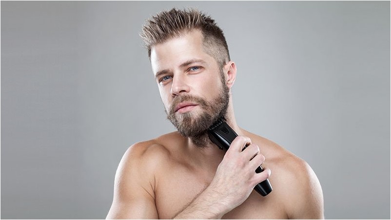Красивый бородатый мужчина стрижет бороду триммером