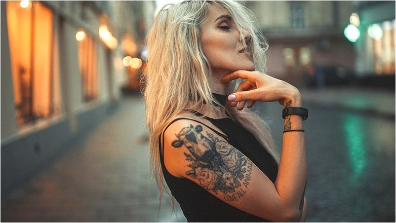 Портрет молодой женщины с татуировкой на плече, стоя на улице города