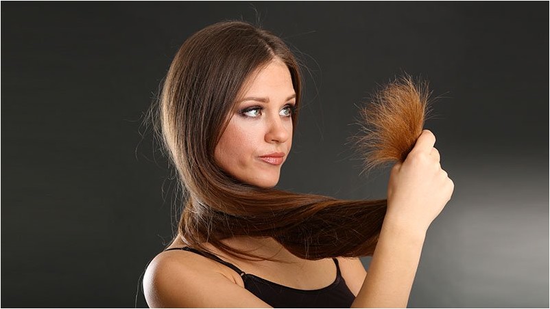 Красивая женщина держит секущиеся кончики ее длинных волос,